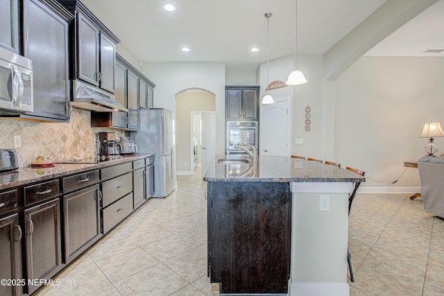 1911 Salt Creek Dr, Fleming Island, FL 32003 - kitchen featuring under cabinet range hood, light tile patterned floors, arched walkways, a sink, and appliances with stainless steel finishes