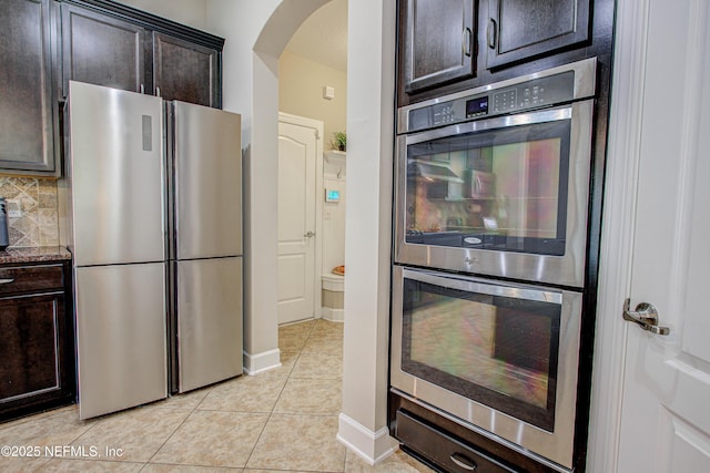 1911 Salt Creek Dr, Fleming Island, FL 32003 - kitchen featuring stone countertops, light tile patterned floors, arched walkways, dark brown cabinetry, and appliances with stainless steel finishes
