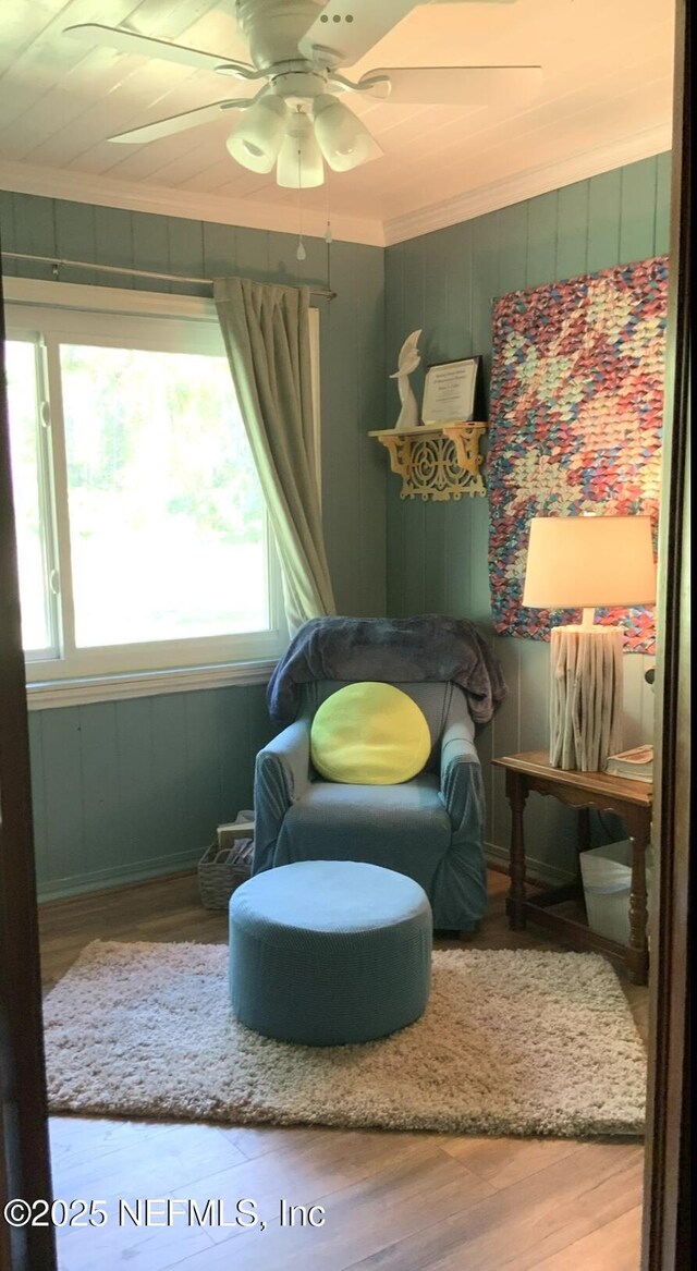 living area with wood finished floors, crown molding, baseboards, and a ceiling fan
