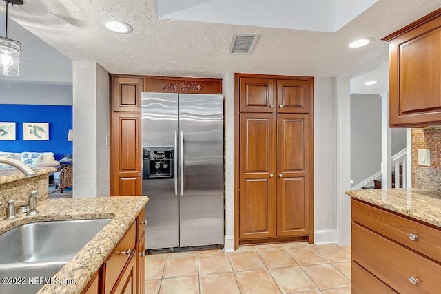 kitchen with visible vents, brown cabinets, light tile patterned floors, a sink, and stainless steel fridge