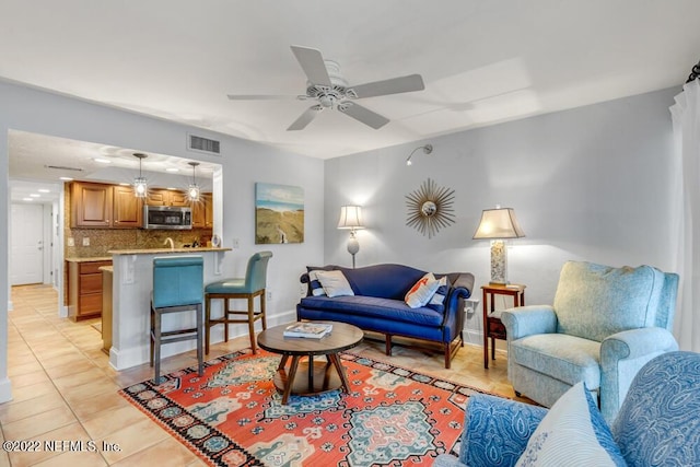 living area with light tile patterned floors, ceiling fan, visible vents, and baseboards