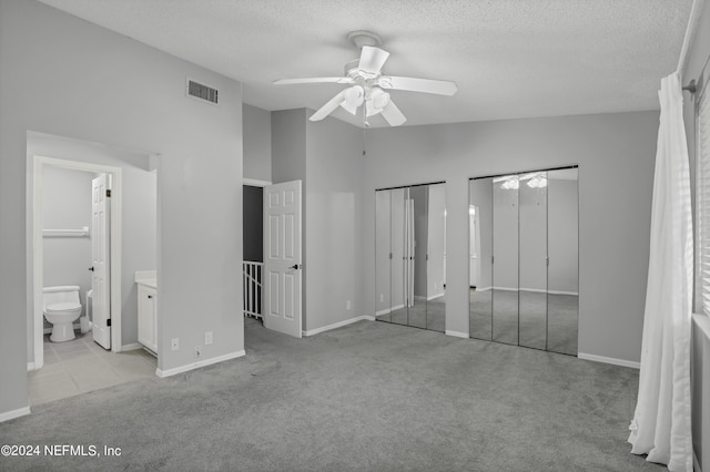 unfurnished bedroom featuring two closets, connected bathroom, a textured ceiling, light colored carpet, and visible vents