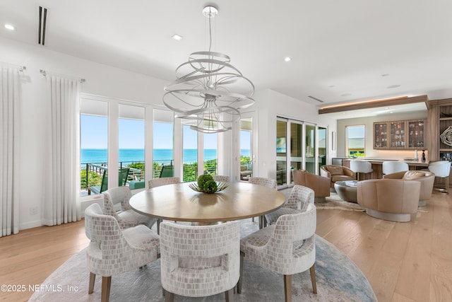 dining space featuring a water view, light wood finished floors, a chandelier, and visible vents