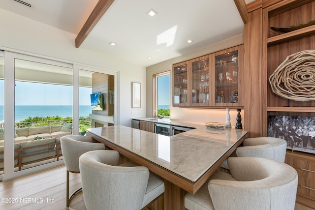 bar featuring a water view, plenty of natural light, beam ceiling, and light wood-type flooring