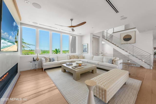 living room featuring plenty of natural light, a ceiling fan, light wood-style flooring, and stairway