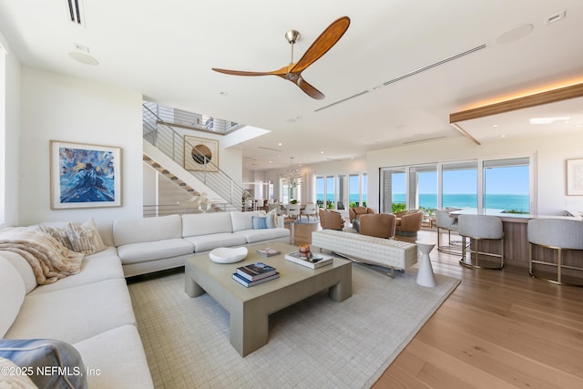 living room with ceiling fan, stairs, wood finished floors, a water view, and visible vents