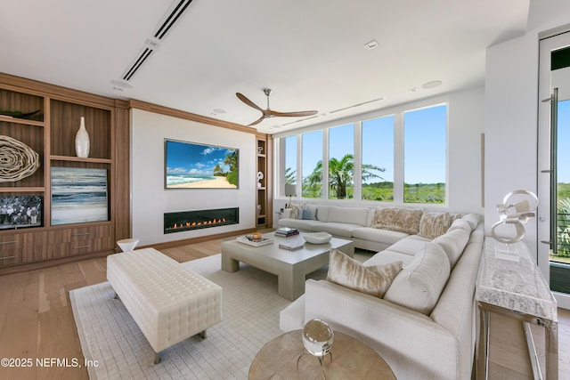 living area with light wood-style floors, ceiling fan, a glass covered fireplace, and a healthy amount of sunlight