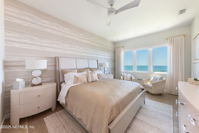 bedroom featuring a water view, a ceiling fan, visible vents, and wood finished floors