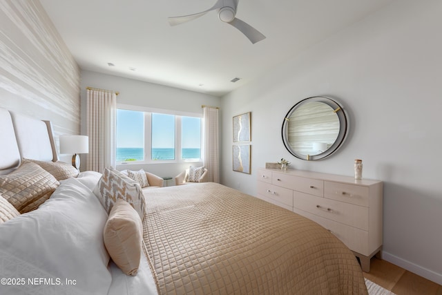 bedroom with visible vents, light wood-style floors, baseboards, a water view, and a ceiling fan
