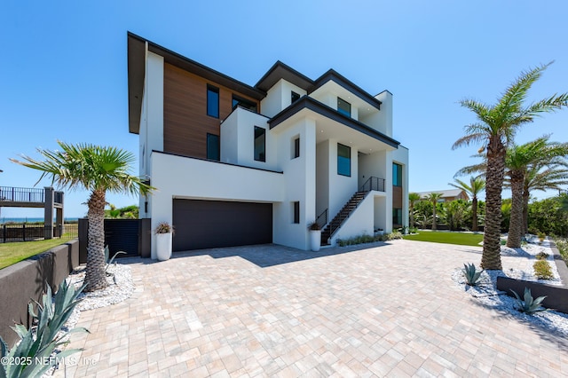 contemporary house with a garage, stairway, decorative driveway, fence, and stucco siding