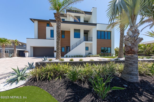 contemporary house featuring concrete driveway, an attached garage, stairway, and stucco siding