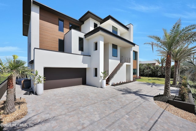 contemporary home featuring stairs, stucco siding, an attached garage, and decorative driveway