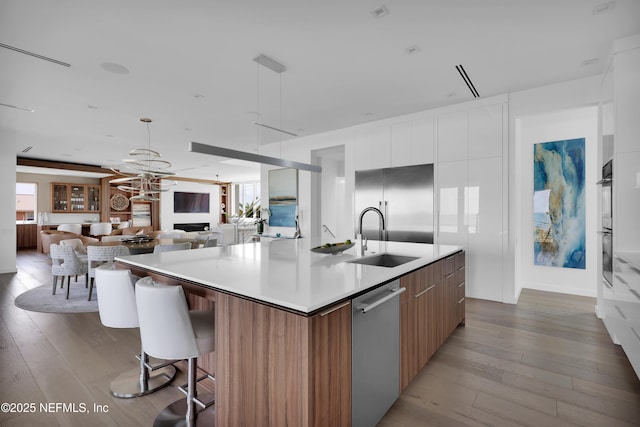 kitchen with a large island, appliances with stainless steel finishes, modern cabinets, light wood-type flooring, and a sink