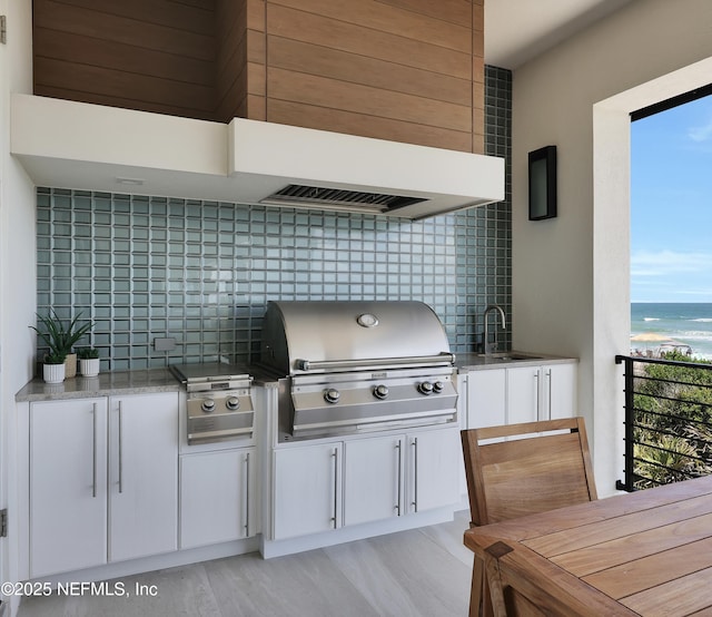 kitchen with light stone countertops, a sink, white cabinetry, backsplash, and a water view