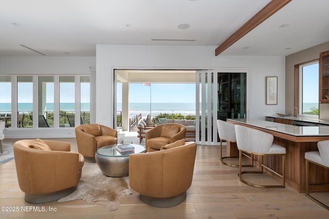 living room with a water view, beamed ceiling, and light wood-style flooring