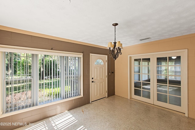 entrance foyer featuring an inviting chandelier, speckled floor, concrete block wall, visible vents, and a textured ceiling