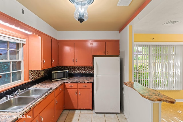 kitchen with a sink, light tile patterned flooring, stainless steel microwave, backsplash, and freestanding refrigerator
