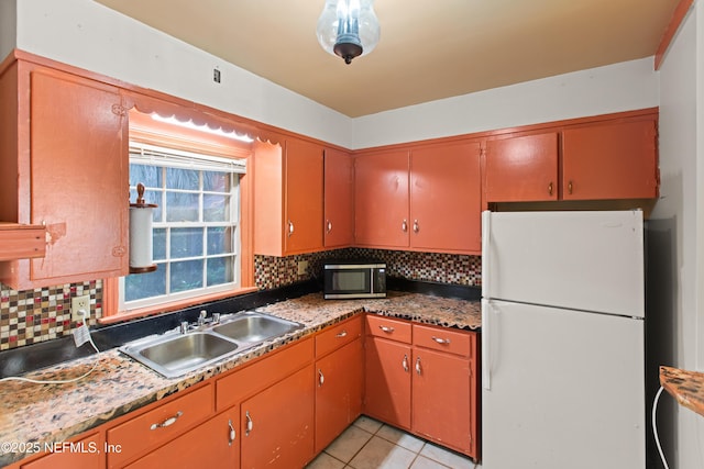 kitchen featuring decorative backsplash, freestanding refrigerator, a sink, and stainless steel microwave
