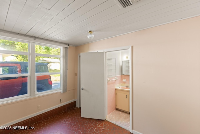 unfurnished bedroom featuring a sink, visible vents, baseboards, dark tile patterned flooring, and connected bathroom