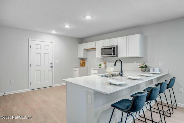 5454 Amazon Ave, Jacksonville, FL 32254 - kitchen featuring white cabinets, a kitchen breakfast bar, a sink, stainless steel microwave, and a peninsula