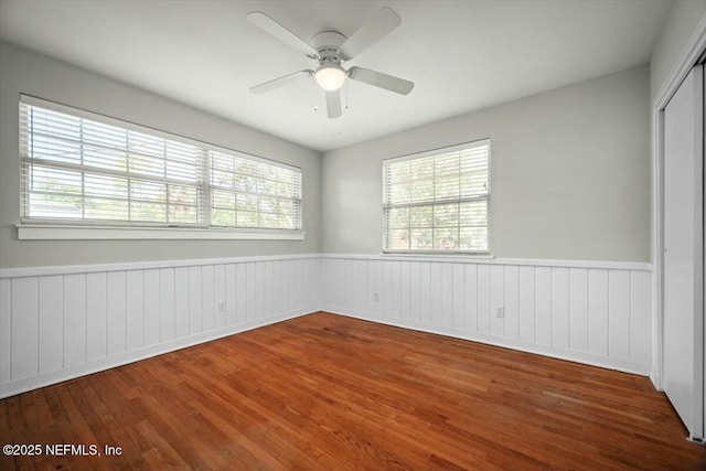 unfurnished room featuring wainscoting, wood finished floors, and a wealth of natural light