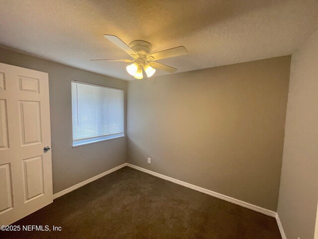 empty room with dark carpet, a ceiling fan, and baseboards