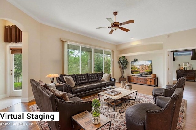 living area featuring crown molding, wood finished floors, baseboards, arched walkways, and a ceiling fan
