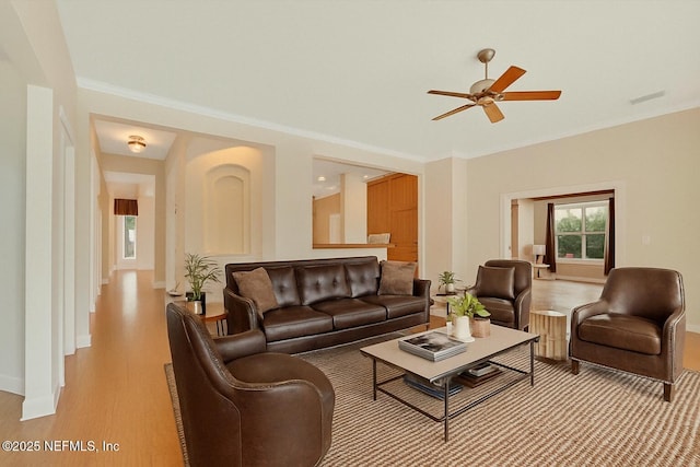living room featuring crown molding, light wood-style flooring, a ceiling fan, baseboards, and visible vents