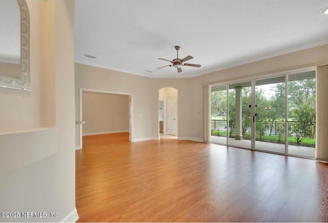 spare room featuring arched walkways, a ceiling fan, baseboards, and light wood finished floors