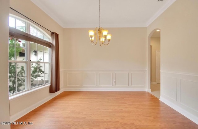 spare room featuring crown molding, arched walkways, light wood finished floors, a notable chandelier, and a decorative wall