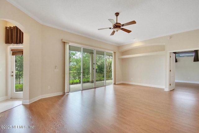 empty room featuring crown molding, ceiling fan, arched walkways, light wood-style flooring, and baseboards
