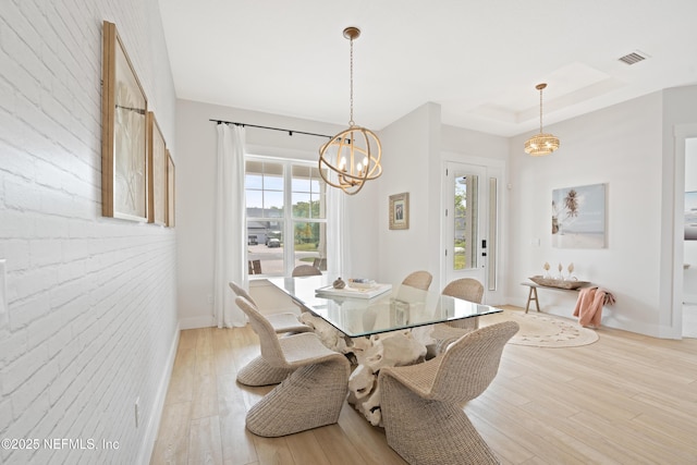 dining space with visible vents, light wood-type flooring, baseboards, an inviting chandelier, and a tray ceiling