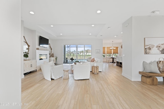 living room featuring a glass covered fireplace, light wood-style flooring, recessed lighting, baseboards, and a tray ceiling