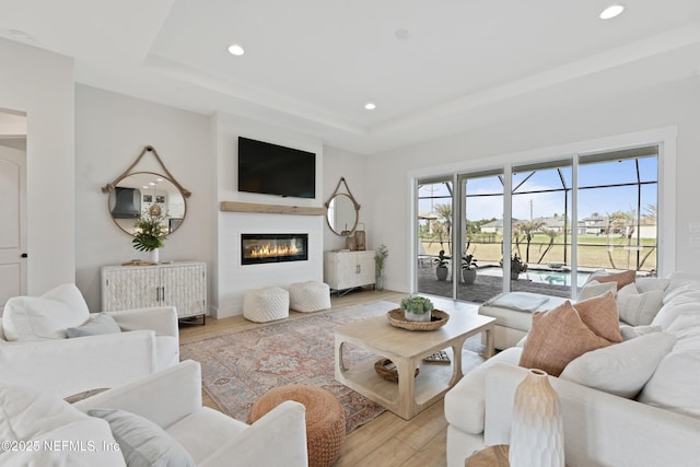 living area with a tray ceiling, recessed lighting, and light wood-style flooring