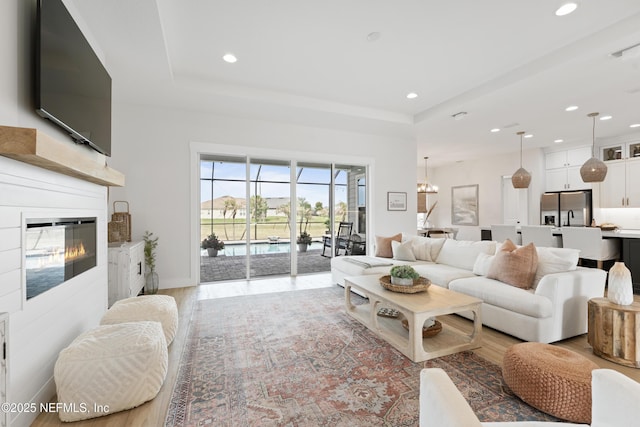living area with light wood-style floors, a raised ceiling, and recessed lighting