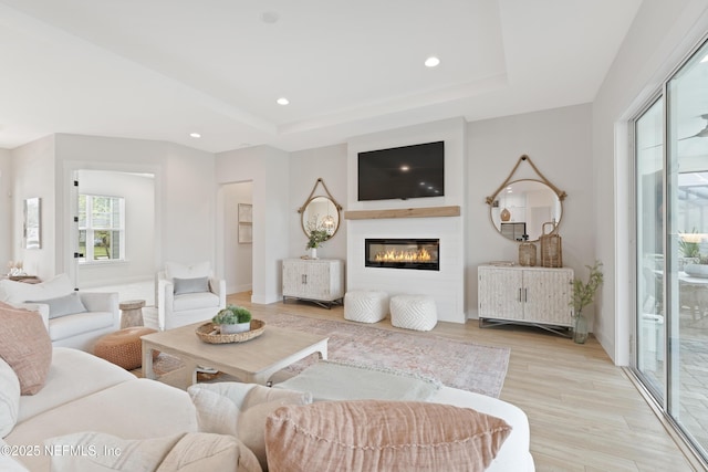 living room featuring recessed lighting, a raised ceiling, light wood-style flooring, and a glass covered fireplace