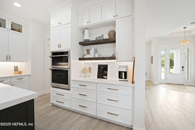 kitchen featuring open shelves, stainless steel double oven, light wood-style flooring, white cabinetry, and baseboards