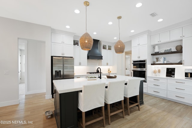 kitchen with visible vents, light countertops, custom exhaust hood, stainless steel appliances, and light wood-style flooring