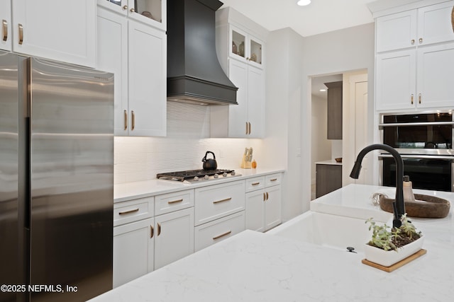 kitchen featuring a sink, stainless steel appliances, white cabinetry, tasteful backsplash, and custom exhaust hood