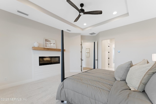 bedroom with carpet flooring, a raised ceiling, a glass covered fireplace, baseboards, and visible vents