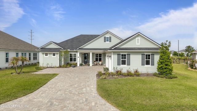 view of front facade with roof with shingles, decorative driveway, and a front yard