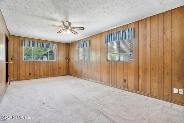 carpeted empty room featuring a ceiling fan, wooden walls, and a textured ceiling