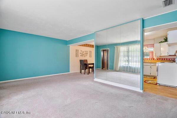 unfurnished living room with light colored carpet, visible vents, and baseboards