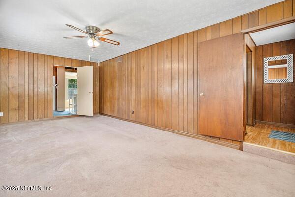 carpeted empty room featuring a ceiling fan and wood walls