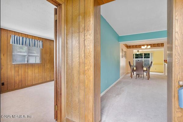 hallway with wood walls, carpet, an inviting chandelier, and baseboards