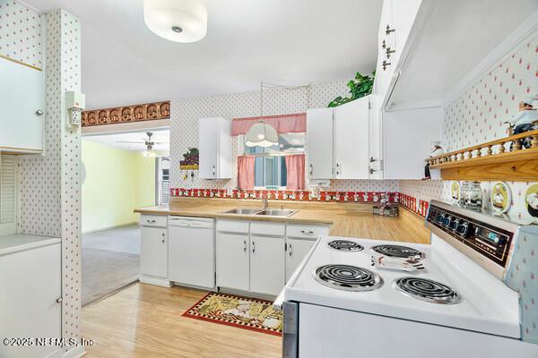 kitchen featuring white cabinets, a sink, wallpapered walls, and white appliances