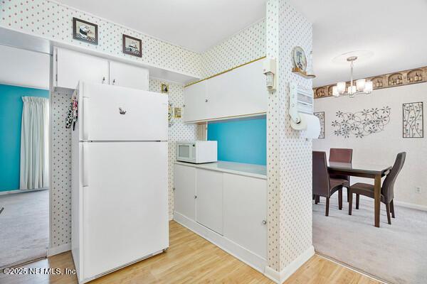 kitchen with an inviting chandelier, white appliances, white cabinetry, light wood-style flooring, and baseboards