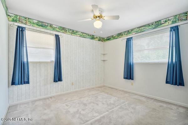 carpeted empty room featuring a ceiling fan, a wealth of natural light, and baseboards