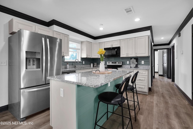 kitchen with appliances with stainless steel finishes, ornamental molding, wood finished floors, and visible vents