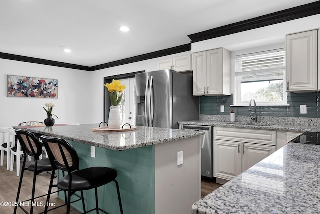kitchen with crown molding, a sink, a breakfast bar area, stainless steel appliances, and a kitchen island